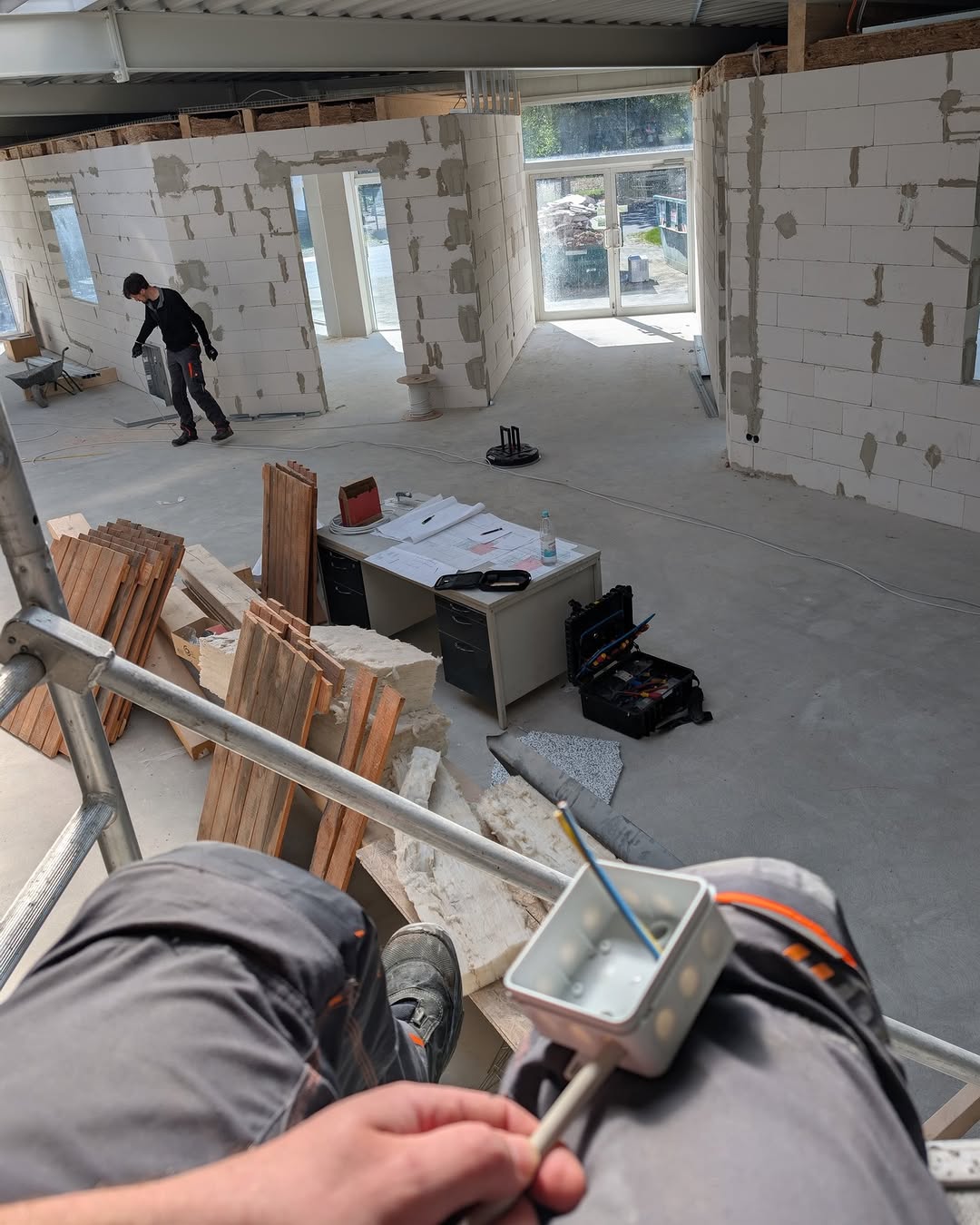 Großbaustelle: ein Kollege zieht Kabel, im Vordergrund die Arbeit an einer Dose